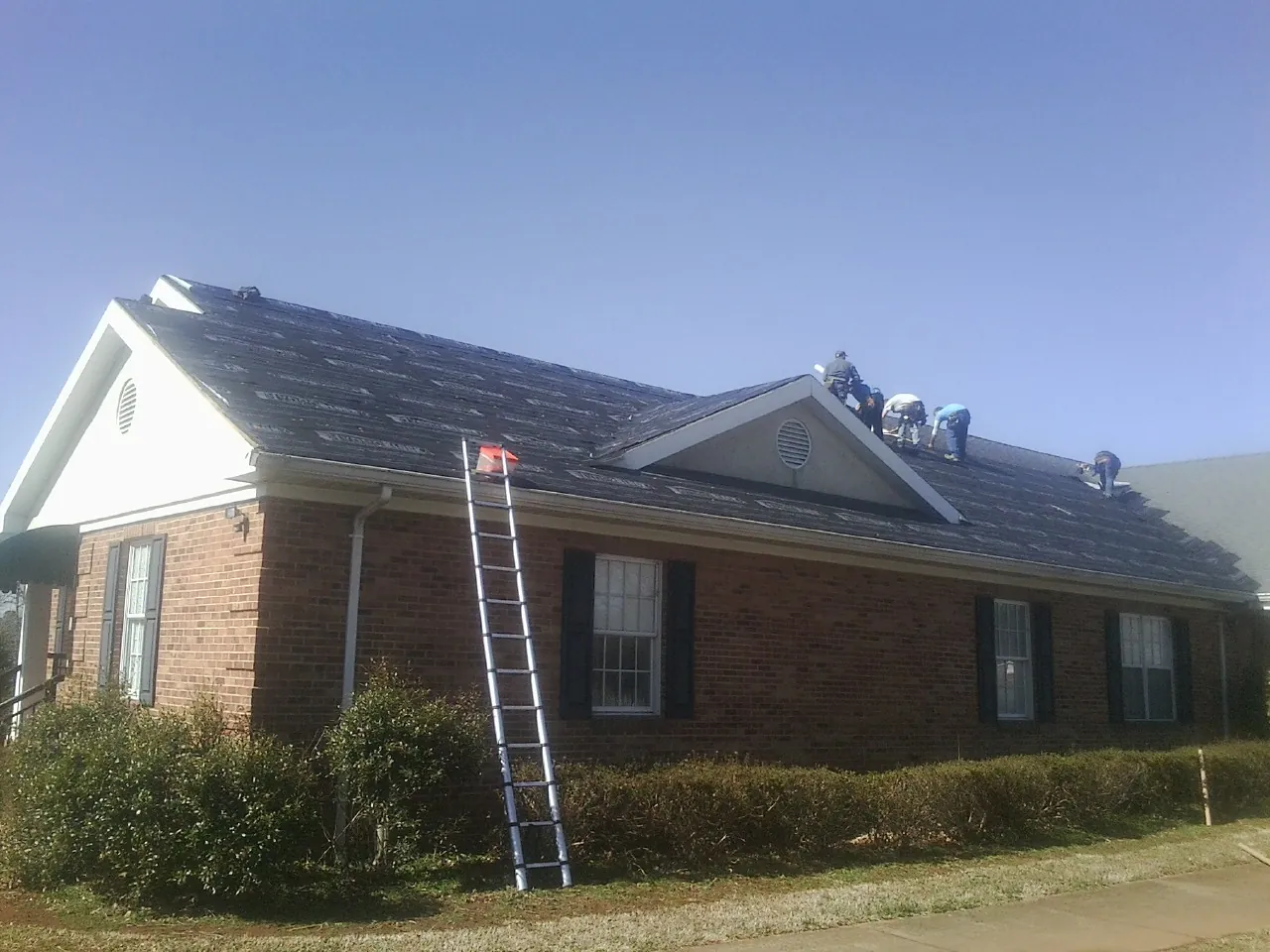 Crew tearing shingles off a brick ranch roof with a ladder set — Emergency Roof Repair work by our crew in New Plymouth