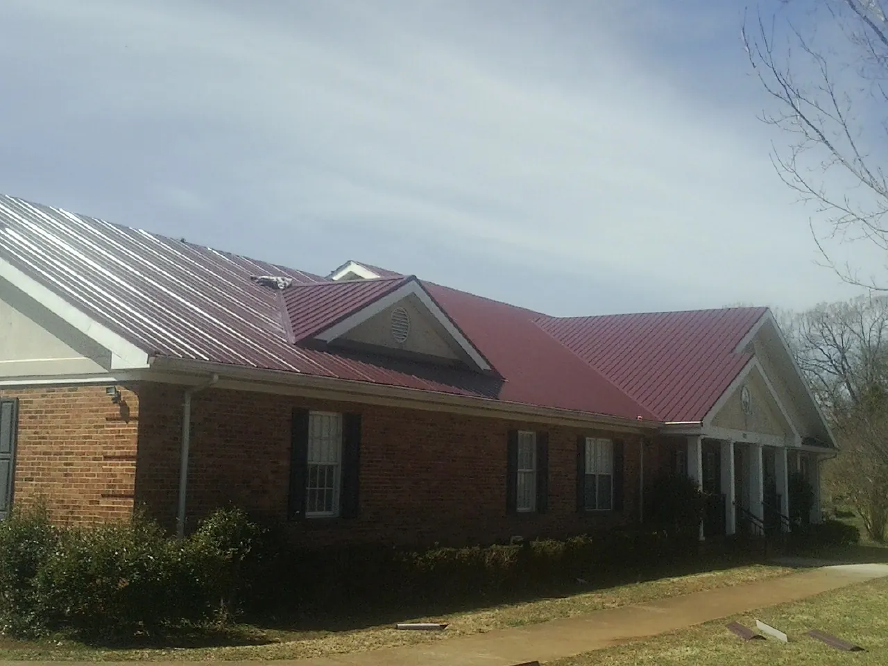 Red metal roof with gabled entries on a long brick building, from a Hail Damage Roof Repair job in New Plymouth