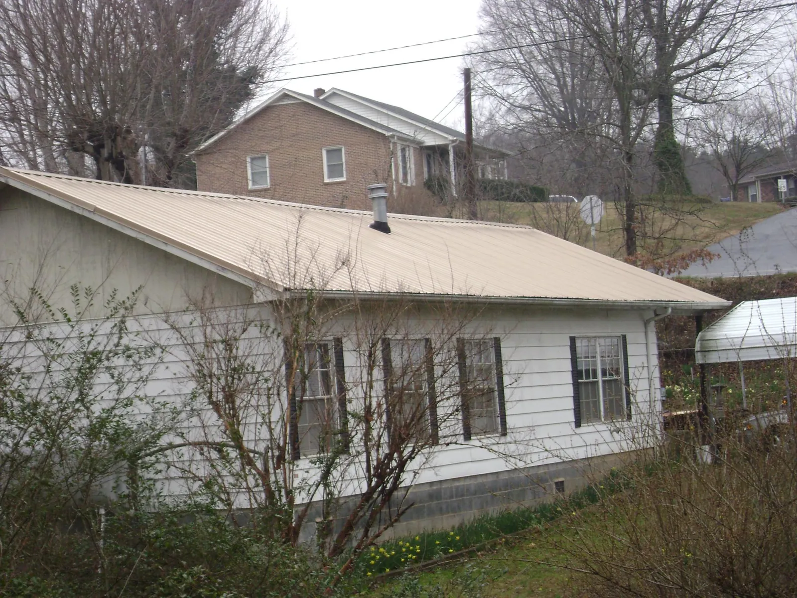 Tan metal roof on a white sided house set into a hillside — Commercial Roofing by Roofing Brothers in New Plymouth