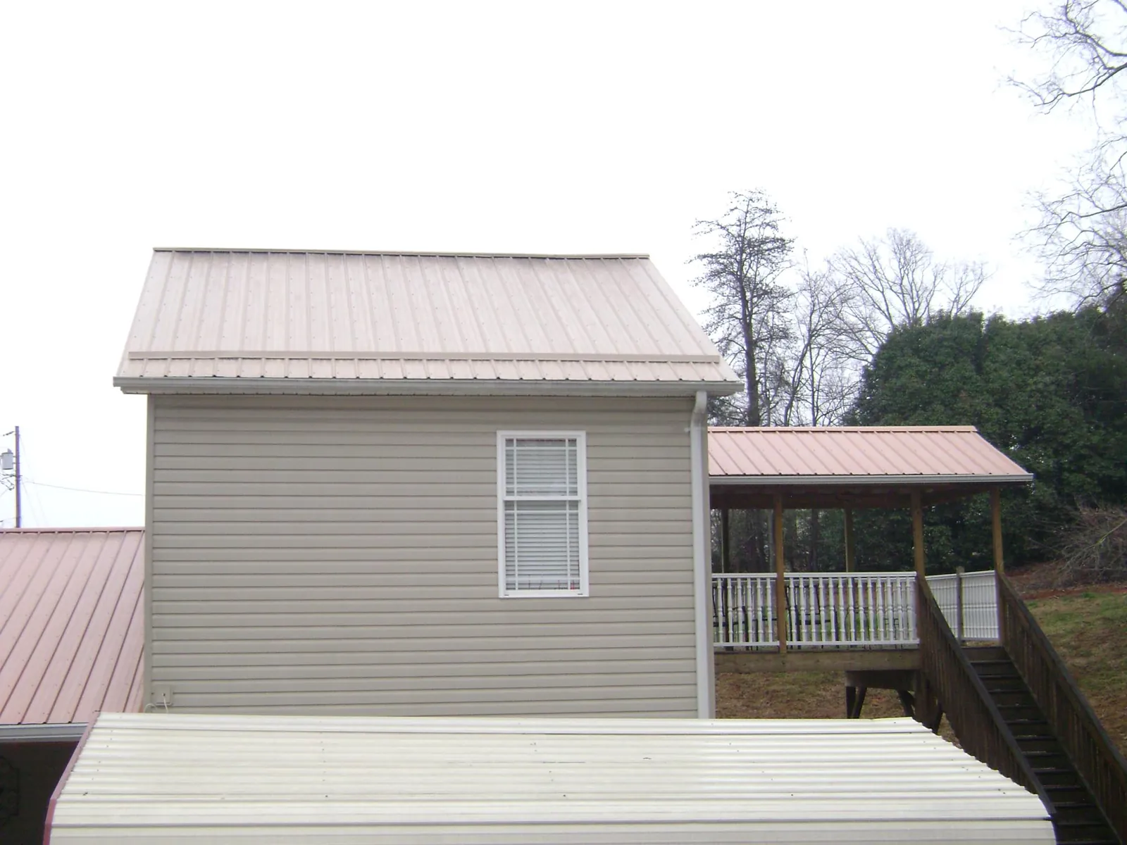 Tan metal roofs on a two story addition and attached porch, from a Roof Replacement job in New Plymouth